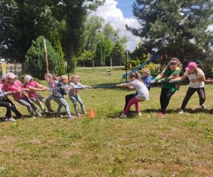 Zdjęcie przedstawia grupę dzieci bawiące się w przeciąganie liny na świeżym powietrzu.