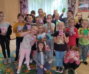 Zdjęcie przestawia grupę dzieci prezentującą swoje prace plastyczne wykonane w trakcie zabaw wakacyjnych.