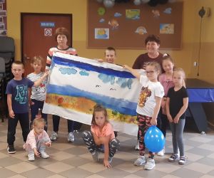 Zdjęcie przedstawia dzieci pozujące wraz z panią, trzymając wykonany na prześcieradle obraz.