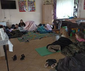 Na zdjęciu są widoczne dzieci śpiące na karimatach wewnątrz budynku.