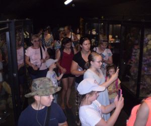 Grupa osób zwiedzająca muzeum, robiąca zdjęcia i oglądająca zgromadzone artefakty.