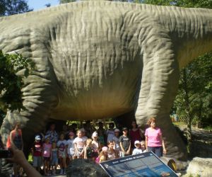Na zdjęciu znajduje się grupa osób pozującą do zdjęcia pod dużym dinozaurem.