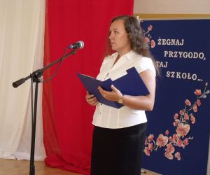 Nauczycielka - konferansjer na tle biało-czerwonej flagi i tablicy dekoracyjnej