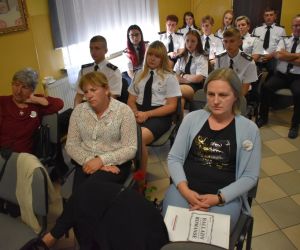 Na zdjęciu znajduje się grupa osób siedząca na krzesłach wewnątrz budynku.