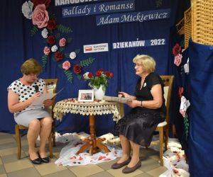 Na zdjęciu widoczne są dwie kobiety siedzące przy stoliku czytające wiersze.