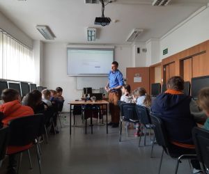 Uczniowie siedzą i słuchają wykładu o czujnikach, prowadzący demonstruje działanie Ozobota.