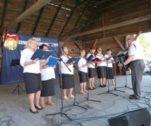 Kobiety stojące na scenie. Przed nimi mikrofony. W rękach trzymają teczki. 