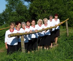 Członkinie zespołu śpiewaczego i Klubu Seniora BIEDRONKI. Ubrane uroczyście, pozują do zdjęcia w otoczeniu natury.