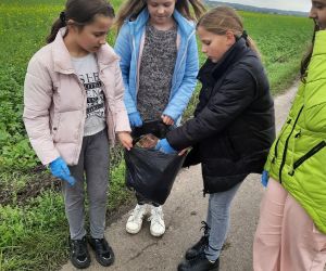 Dziewczynki wrzucają śmieci do worka, który jest już wypełniony po brzegi.