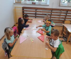 Przedszkolaki przy stoliku układają kolorowe kropki na papierowych czapeczkach