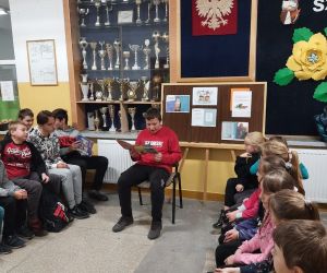 Chłopiec w czerwonej bluzie czyta książkę, dzieci siedzą i słuchają