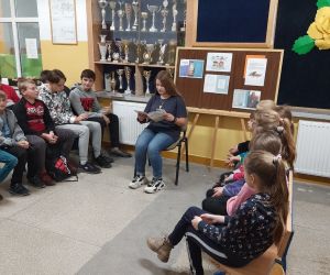 Uczennica klasy ósmej siedzi i czyta książkę, uczniowie słuchają.