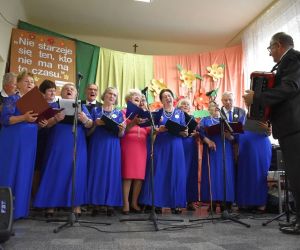 Kobiety w błękitnych sukienkach, mężczyźni w garniturach. Występują na 