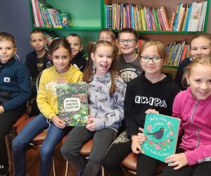 Na zdjęciu widać pozującą grupę dzieci, które trzymają w dłoniach książki o ptakach. W tle widoczny jest regał z książkami.