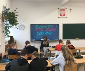 Dziewczynka z klasy siódmej siedzi przodem do klasy i czyta książkę