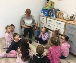Nauczycielka czyta książkę siedzącym wokół niej dzieciom z klasy pierwszej