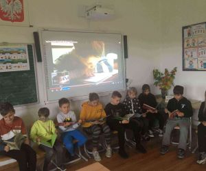 Dzieci z klasy trzeciej siedzą obok siebie na krzesełkach i czytają książeczki