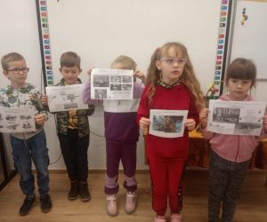 Uczniowie stoją przy tablicy i trzymają w dłoniach obrazki z drzewem i jego budową.
