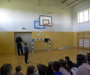 Policjant i chętny uczeń demonstrują  bezpieczne przechodzenie przez jezdnię