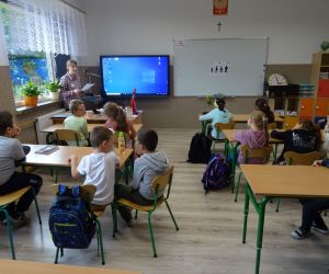 Dzieci razem z osobą prowadzącą zajęcia, w klasie.