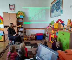 Dzieci razem z osobą prowadzącą zajęcia, w klasie.