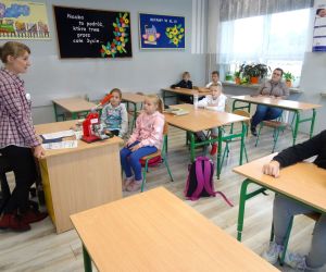 Dzieci razem z osobą prowadzącą zajęcia, w klasie.