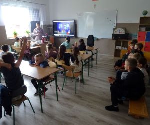 Dzieci razem z osobą prowadzącą zajęcia, w klasie.