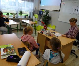 Dzieci razem z osobą prowadzącą zajęcia, w klasie.