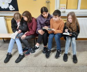 Uczniowie siedzą na ławce i czytają książki