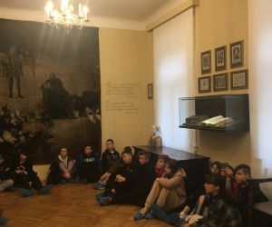 Uczniowie siedzący na podłodze słuchają przewodnika