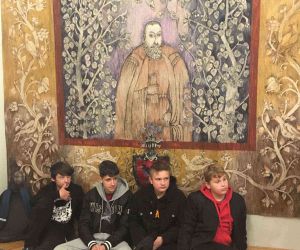 Czworo uczniów siedzi na podłodze przed gobelinem przedstawiającym postać Jana Kochanowskiego