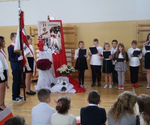 Poczet sztandarowy na tle dekoracji i dzieci występujące w apelu