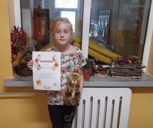 Uczennica trzyma w ręku dyplom i nagrodę  otrzymaną za udział w konkursie o jesieni