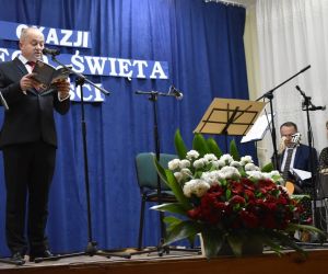 Osoba występuje na scenie. Osoby prowadzące koncert znajdują się z boku.