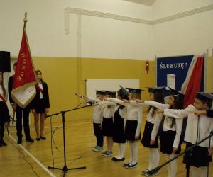 Uczniowie klasy pierwszej w biretach i strojach galowych składają ślubowanie na sztandar szkoły