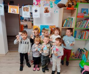 Na zdjęciu widoczna jest grupa dzieci, trzymająca w dłoniach pluszowe misie. W tle regał z książkami.