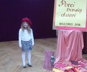 Dziewczynka, pozuje do zdjęcia na scenie. Tablica z napisem: Turniej Sztuki i Słowa, Poeci bawią dzieci.