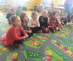 Dzieci siedzą na dywanie i oglądają bajkę.