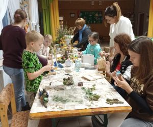 Na zdjęciu widoczne są dzieci i dorośli wykonujące prace plastyczne.