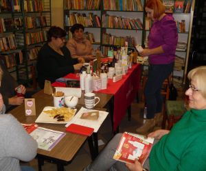 Na zdjęciu widocznych jest kilka osób siedzących na krzesłach w otoczeniu regałów z książkami.