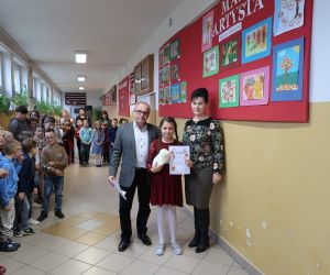 Laureatka konkursu prezentuje nagrodę i pamiątkowy dyplom, obok stoi dyrektor i nauczycielka