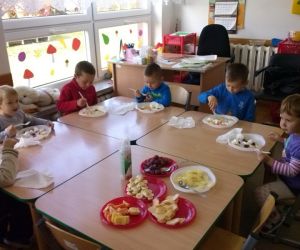 Dzieci siedzą przy stole, jedzą pokrojone warzywa i owoce