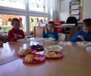 Dzieci siedzą przy stole, jedzą pokrojone warzywa i owoce