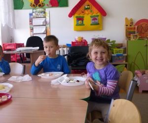 Dzieci siedzą przy stole, jedzą pokrojone warzywa i owoce