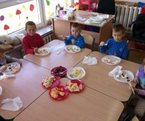 Dzieci siedzą przy stole, jedzą pokrojone warzywa i owoce
