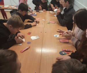 Uczniowie siedzą przy stole i wykonują kartki bożonarodzeniowe