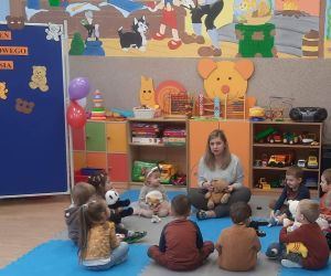Przedszkolaki siedzą w kole z nauczycielką i trzymają w dłoniach swoje misie