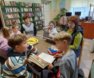 Zdjęcie przedstawia grupę dzieci znajdujących się w bibliotece, czytające książki.