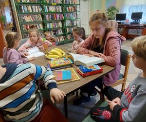 Zdjęcie przedstawia dzieci znajdujące się w bibliotece, czytające książki. 