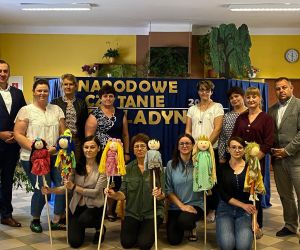 Na zdjęciu znajduje się  grupa ludzi, którzy brali udział przedstawieniu  kukiełkowym pt. „Balladyna”.
Cztery osoby trzymają w rękach kukiełki. Za grupą znajduje się  niebieski parawan, na którym są złote napisy.
